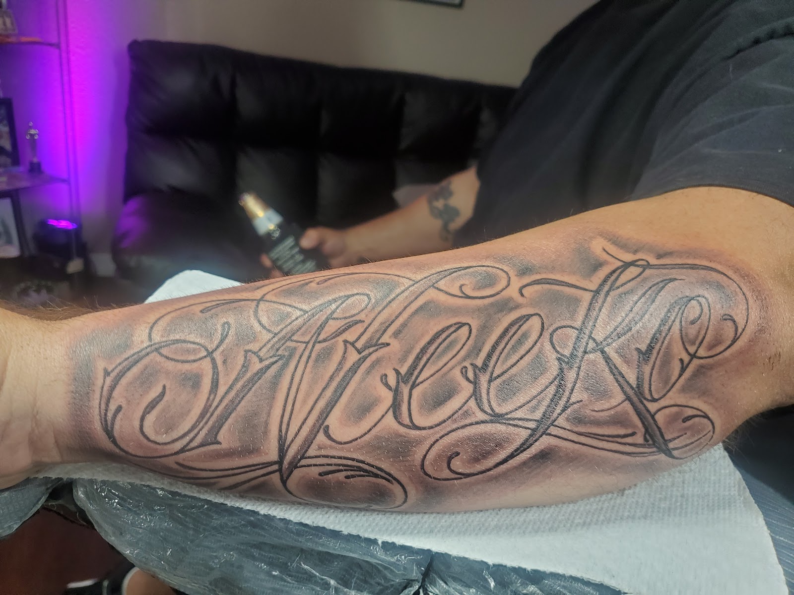 Freshly tattooed script lettering with soft smoke shading across a forearm.
