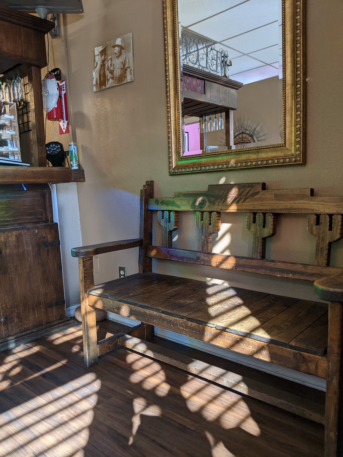 Wooden bench with saguaro cactus cutouts under a gold framed mirror, afternoon light across the floor.