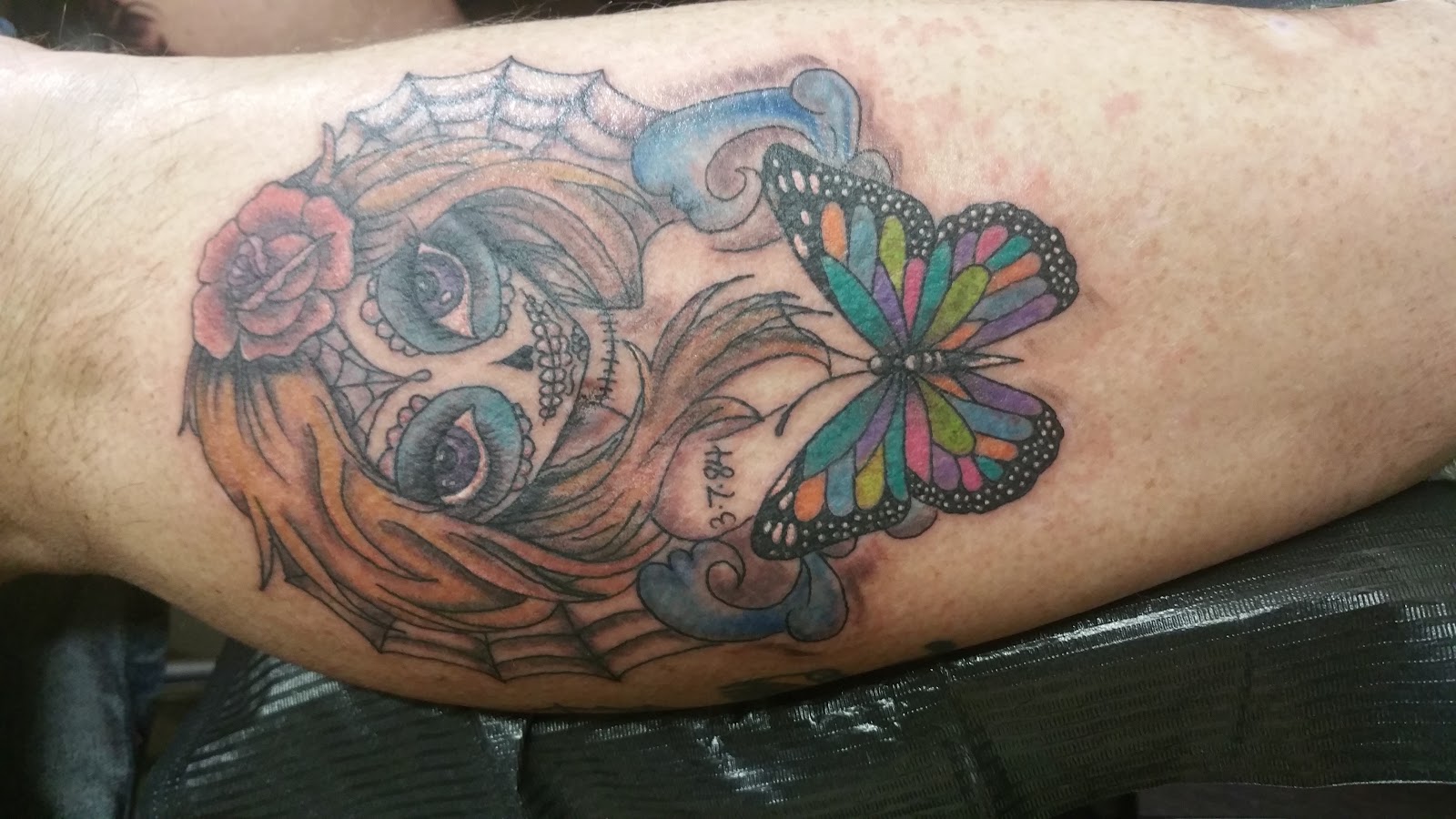 Color tattoo of a sugar skull woman with a rose in her hair and a rainbow winged butterfly.