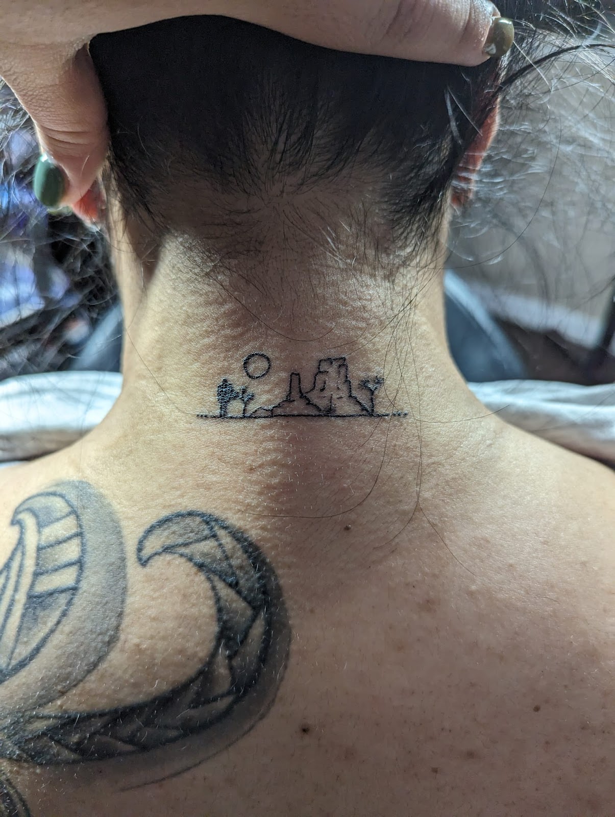 Small fine line desert scene with a saguaro tattooed at the base of the neck.