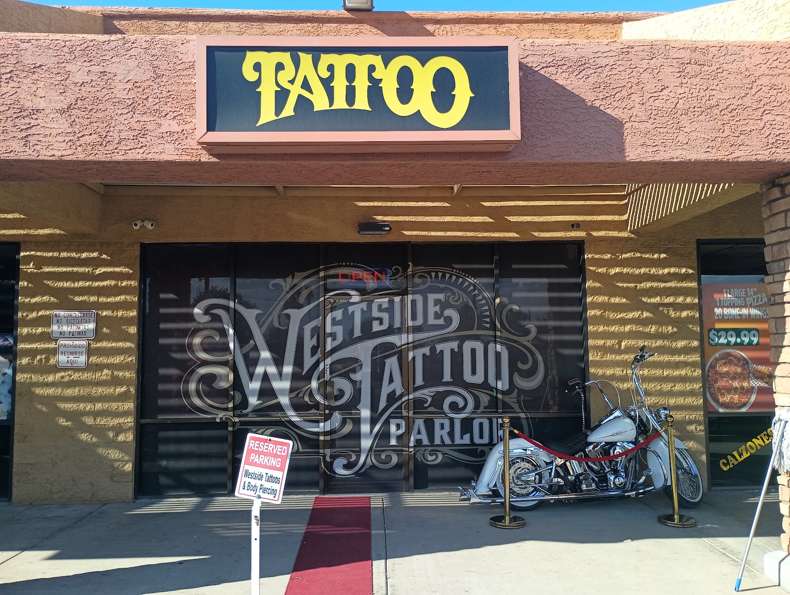 Westside Tattoo storefront in Glendale: a red carpet with gold stanchions leads to the front door, a Harley sits under the ornate window lettering and a yellow TATTOO sign glows above.